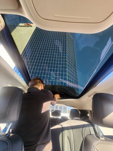 Man adjusting the sunroof of a car with a glass building reflected above.
