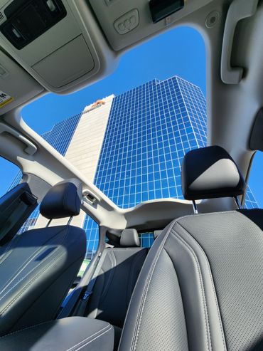 View of a modern office building through the sunroof of a car with leather seats.