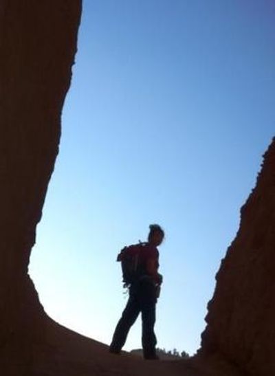 A black and blue silhouette of Pamela in hiking gear standing within a natural made door rock format