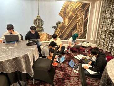 Group of young people studying and working on laptops in a hotel room.