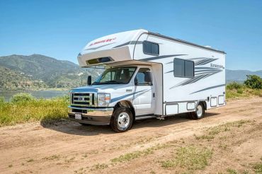 White RV parked on a dirt road with mountainous background.