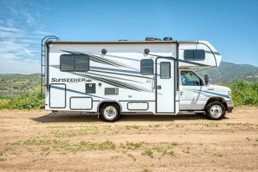 White Sunseeker RV parked on a dirt path with mountains in the background.
