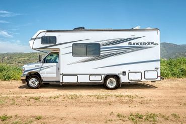 A white Sunseeker RV parked on a dirt road with a mountainous background.