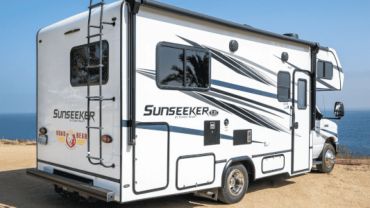 A white Sunseeker RV parked near a body of water under a clear blue sky.