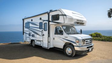 White RV parked near the ocean on a sunny day.