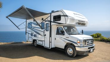 White camper van parked near ocean with awning extended.