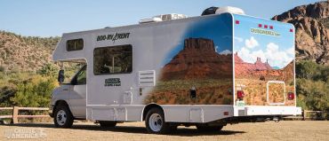 A white RV parked in a desert area with scenic mountain graphics on its side.