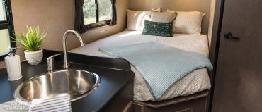 Cozy RV bedroom with a neatly made bed and compact kitchen sink.