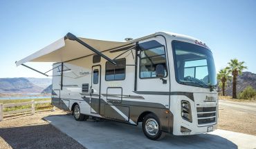 A white and gray motorhome with an extended awning parked outdoors.