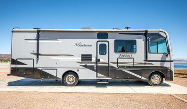 A parked Coachmen Pursuit RV under a clear blue sky.