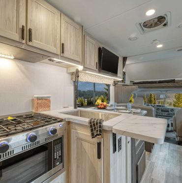 Compact modern RV kitchen with light wood cabinetry.