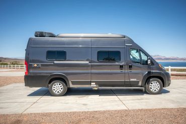 Gray camper van parked on concrete near a body of water.