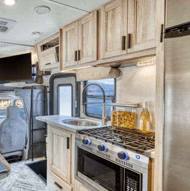 Compact RV kitchen with stove, sink, and storage cabinets.