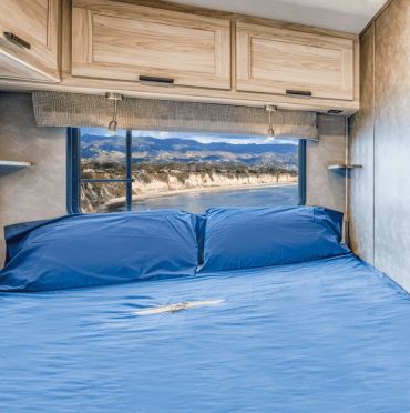 Cozy bed with blue bedding and scenic mountain view through the window.