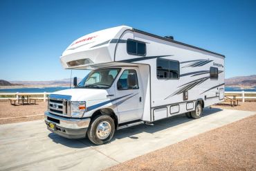 White motorhome parked near a scenic lakeside with clear blue sky.