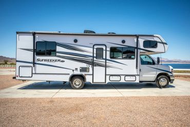 A white Sunseeker RV parked in a desert area with mountains in the background.