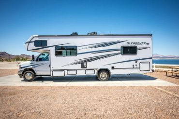 A white Sunseeker RV parked near a lake under a clear blue sky.
