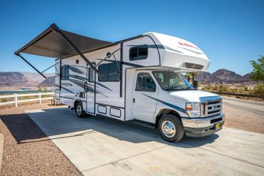 White RV with an extended awning parked on a sunny driveway.