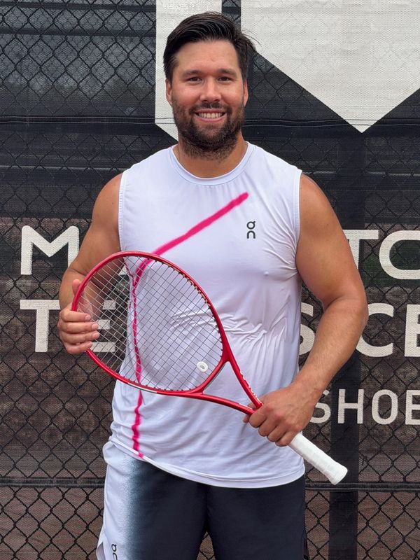Smiling man in sportswear holding a red tennis racket on a tennis court.