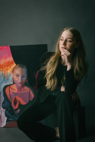 woman artist sitting with a painting behind her