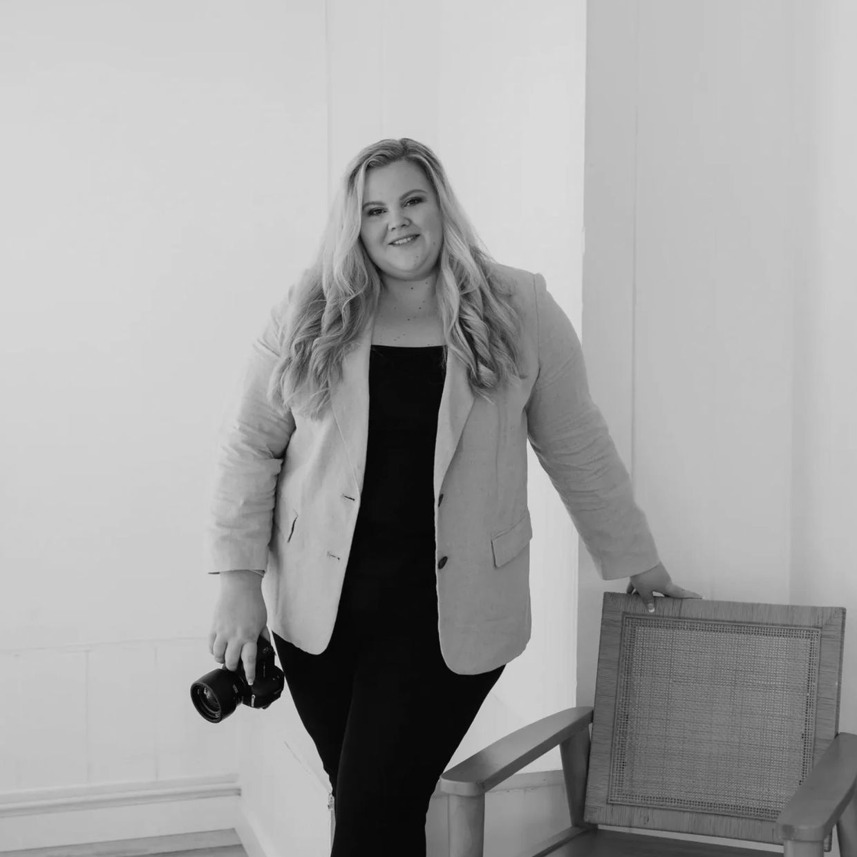 Photo of Whitney Barlow (photographer) standing beside chair and holding a digital camera.
