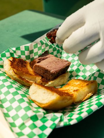 Gloved hand placing meat into a sandwich bun.