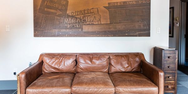 Brown leather couch below a sepia-toned market photo on a white wall.