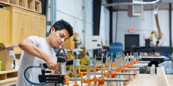 Man using a nail gun to work on a large wooden project in a workshop.