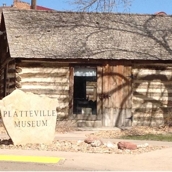 Log cabin house with a Platteeville Museum stone sign.