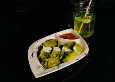 Green dumplings with white sauce and red chutney, served with a drink in a mason jar.