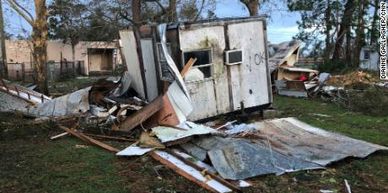 Trailer falling apart with lots of garbage scattered around a yard area