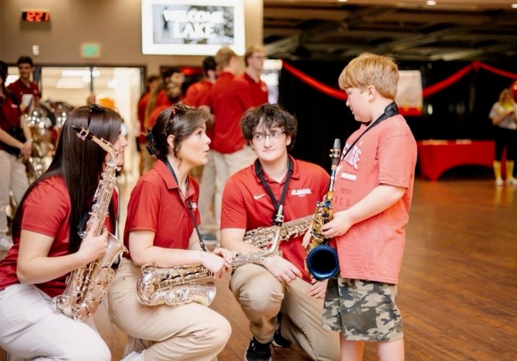Young musicians mentoring a child with a saxophone indoors.