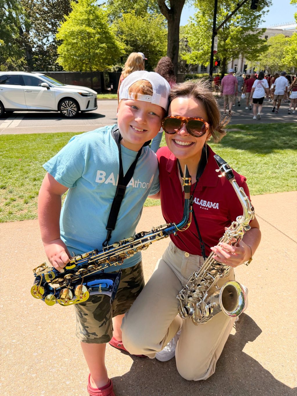 Two smiling saxophone players pose outdoors on a sunny day.