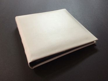 A closed white leather-bound book or album on a dark surface.
