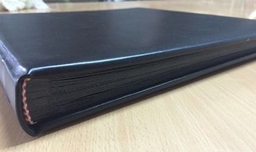 Close-up of a closed black leather-bound book on a wooden surface.