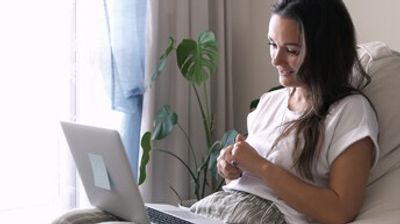 A woman sits comfortably on a couch using a laptop with natural light.