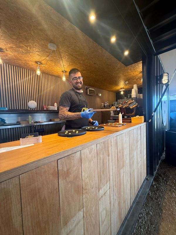 Smiling chef wearing gloves prepares food in a modern kitchen with warm lighting.