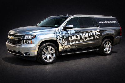 Silver Chevrolet SUV with Ultimate Hail & Dent Co. branding and cracked glass graphic.
