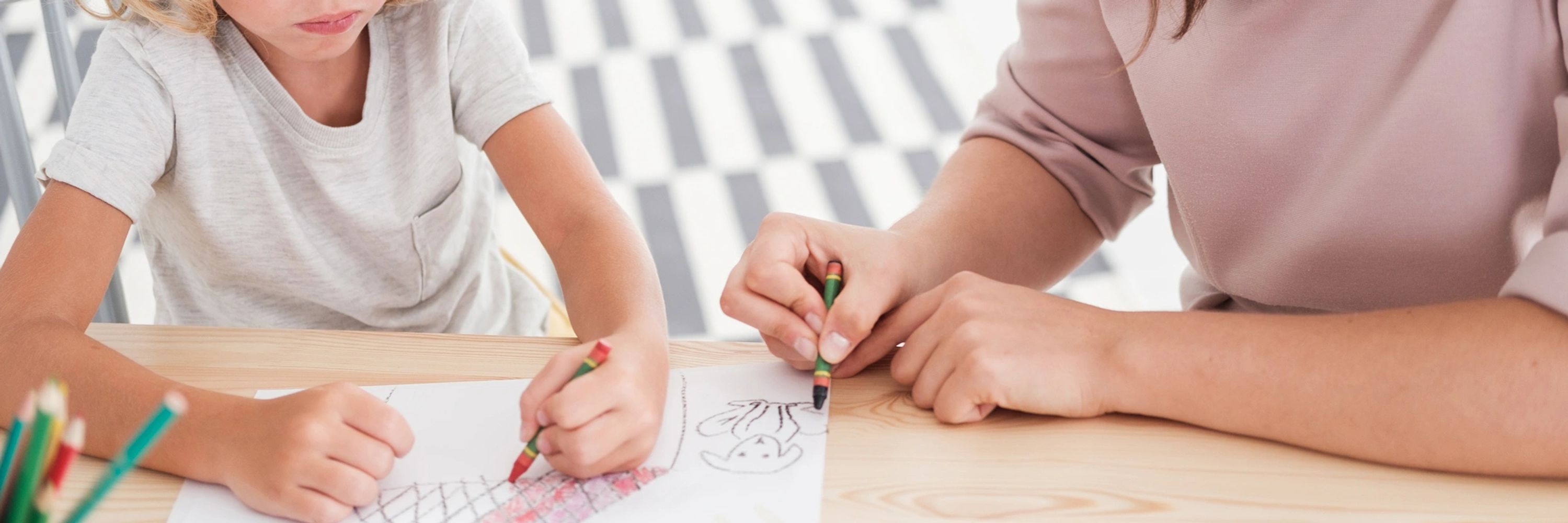 Child and adult coloring together with crayons at a table.