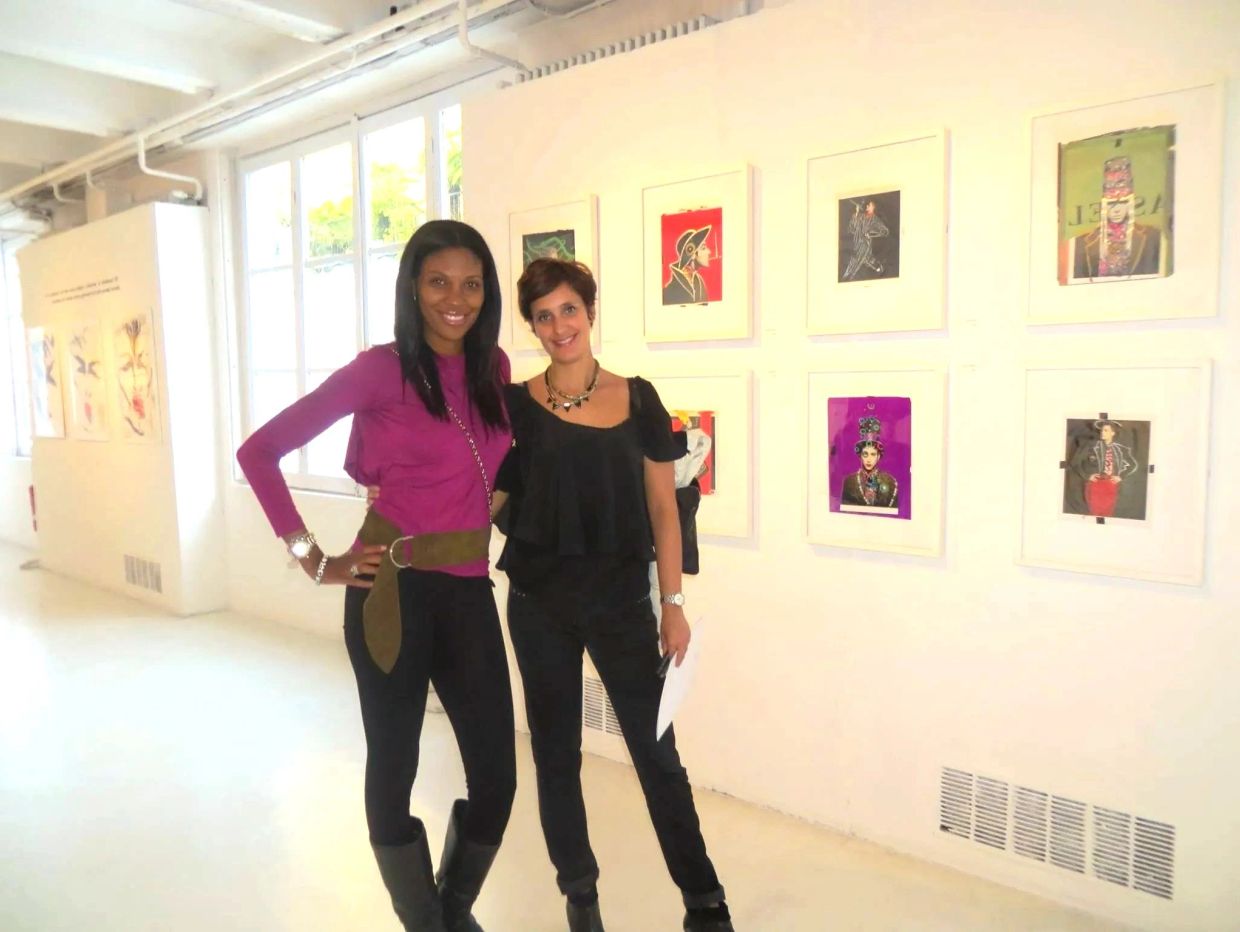 Two women posing inside an art gallery with framed artworks.