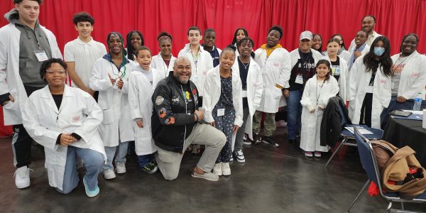 Group photo of diverse children and adults in white lab coats.