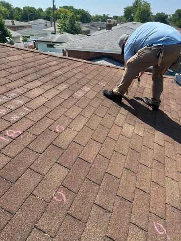 A man inspecting and marking a shingled roof with chalk.