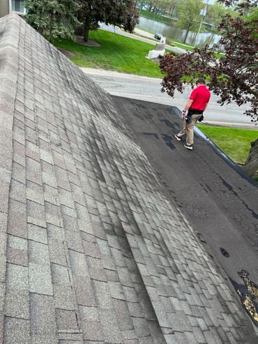 Man in red shirt walking on a flat roof beside a sloped shingle roof.