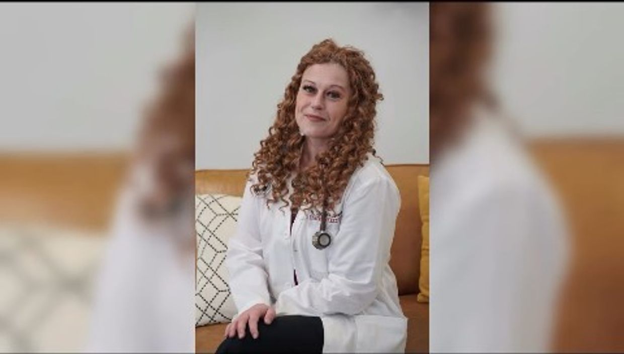Woman doctor with curly hair sitting on a couch, wearing a white coat and stethoscope.