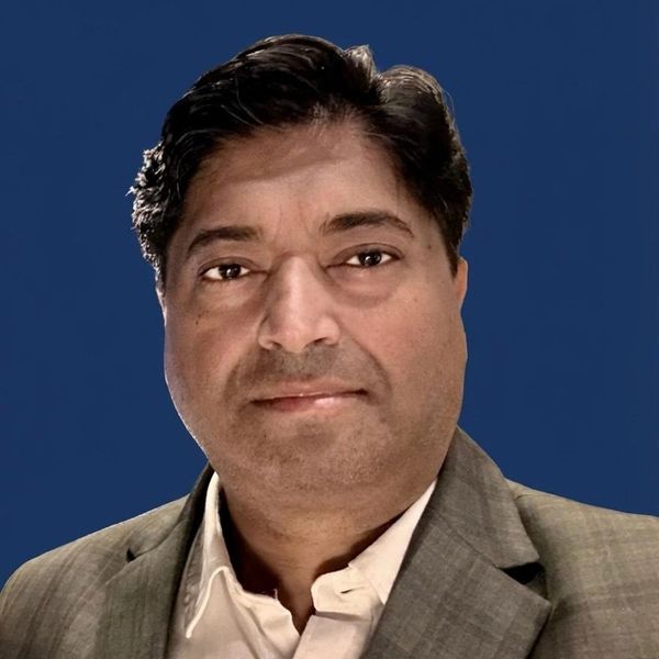 Professional headshot of a man in a suit with a blue background.