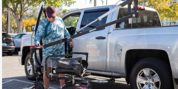 A man uses a vehicle-mounted lift to load a mobility scooter into a pickup truck.