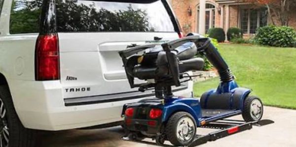 Mobility scooter attached to a white Tahoe SUV on a driveway.