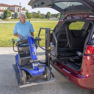 Elderly man using a lift to load a mobility scooter into a vehicle.