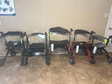 A row of five different rollators lined up indoors against a wall.