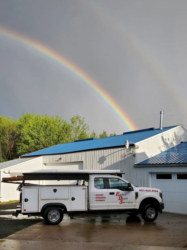 A service truck parked near a building with a vivid rainbow in the sky.
